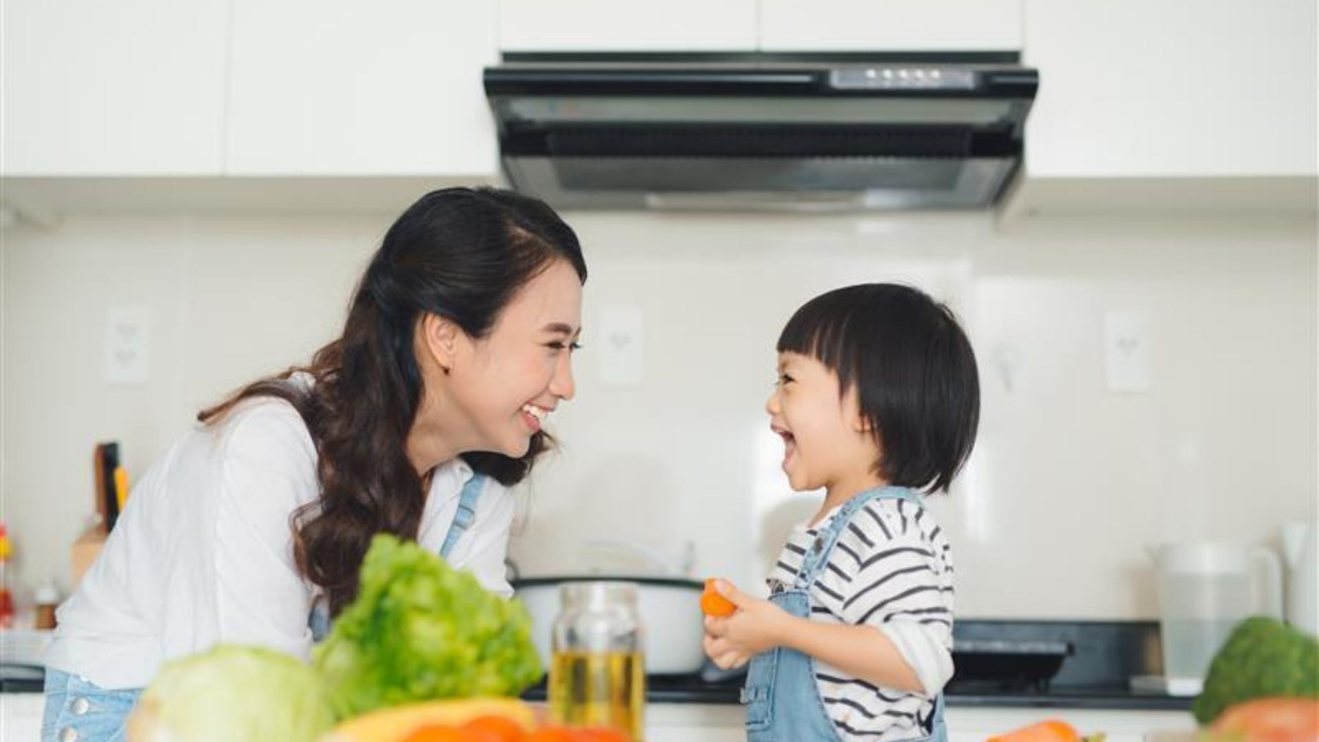 ผู้หญิงยิ้มและเด็กในครัวล้อมรอบด้วยผัก