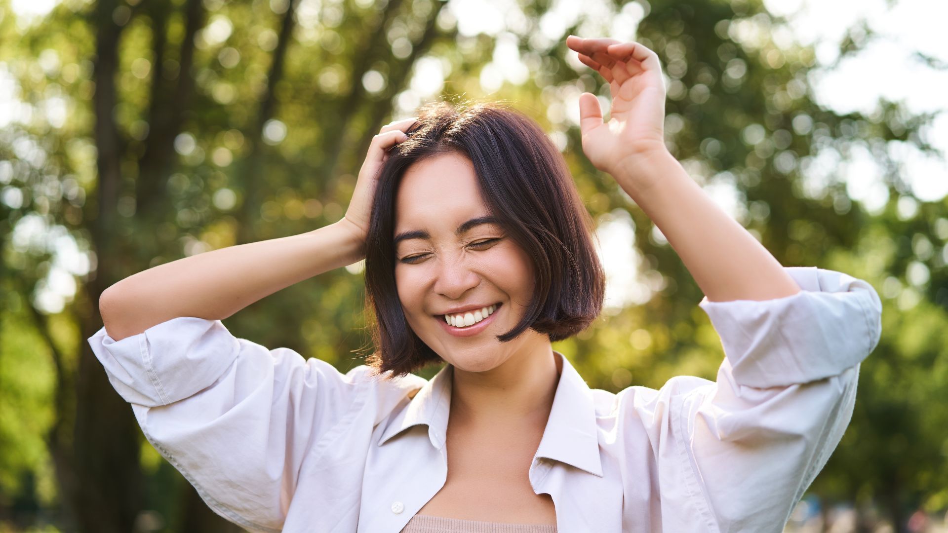 หญิงสาวกำลังยิ้มท่ามกลางธรรมชาติ หลับตา และยกมือขึ้น